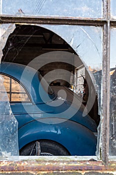 An old Morris Minor car through the broken window of a garage