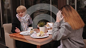 An old mother and daughter discuss bad news sitting in cafe with cups of coffee.