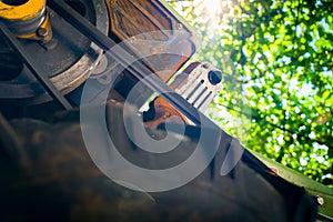 Old motoblock for agriculture, foreshortened view from below against the background of green foliage on a blurred background