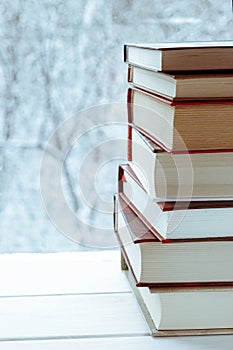 Old multi-colored books stand on a wooden shelf against the backdrop of the winter forest