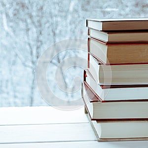 Old multi-colored books stand on a wooden shelf against the backdrop of the winter forest