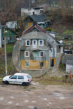 An old multi-storey wooden house in a poor area. A white car is parked near the cottage. Poor living conditions in impoverished