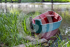 Old multicolored wooden fishing boat tied to a chain near the shore