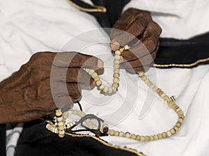 Old Muslim man wearing a black and white traditional garment and holding a rosary in his hands