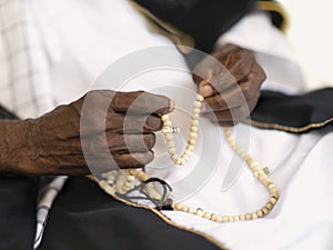 Old Muslim man wearing a black and white traditional garment and holding a rosary in his hands