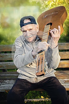 Old mustachioed male rocker sits with an acoustic guitar outdoors in the garden. an old man of Caucasian nationality remembers his