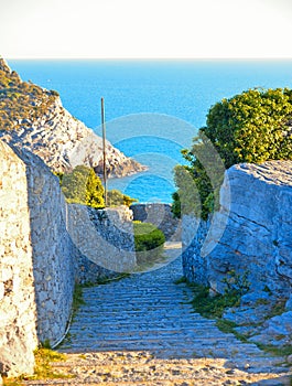 Old narrow stone street and stairs with seascape in background in Portovenere  town. Lord Byron Park and Doria castle on Ligurian