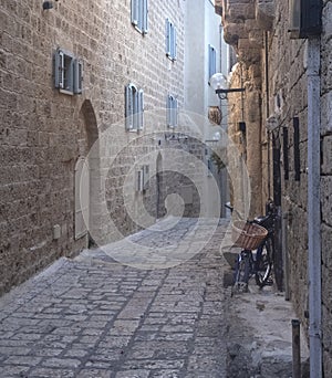 An old narrow street in old Jaffa paved with paving stones with houses with wall of large stones and arched openings