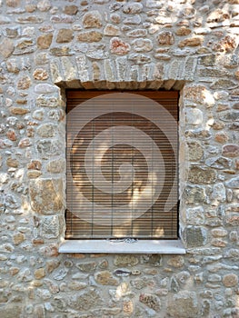Old natural wooden roller shutter on stone wall. Window with closed shutter on old stone facade
