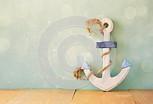 Old nautical anchor on wooden table over wooden aqua background and glitter overlay