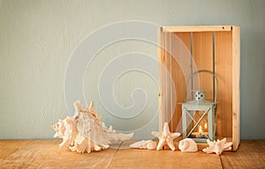 Old nautical lantern and shells on wooden table over wooden aqua background