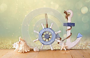 Old nautical wood wheel, anchor and shells on wooden table over abstract glitter background