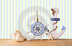 Old nautical wood wheel, anchor and shells on wooden table over retro background.