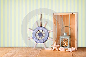 Old nautical wood wheel, anchor and shells on wooden table over retro background