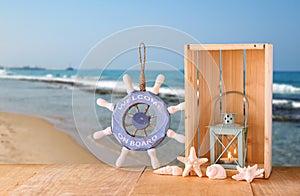 Old nautical wood wheel, anchor and shells on wooden table over sea background