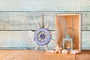 Old nautical wood wheel, anchor and shells on wooden table over wooden background