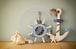 Old nautical wood wheel, anchor and shells on wooden table over wooden background. vintage filtered image