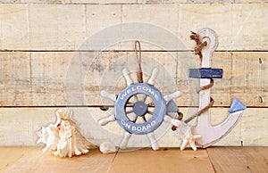 Old nautical wood wheel, anchor and shells on wooden table over wooden background. vintage filtered image
