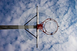 Old neglect basketball backboard with rusty hoop above street court. Blue cloudy sky in bckground. Retro filter