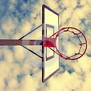 Old neglect basketball backboard with rusty hoop above street court. Blue cloudy sky in bckground. Retro filter