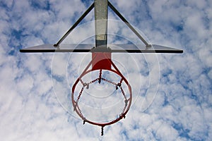 Old neglect basketball backboard with rusty hoop above street court. Blue cloudy sky in bckground. Retro filter