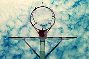 Old neglect basketball backboard with rusty hoop above street court. Blue cloudy sky in bckground. Retro filter