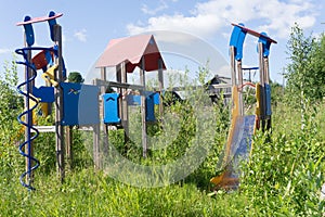 Old neglected playground equipment, overgrown with weeds.