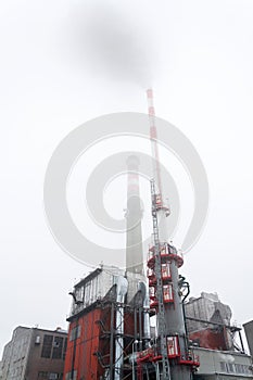 Old a new chimneys at heating plant covered in fog, cloudy winter day, low angle view, energy production, climate change