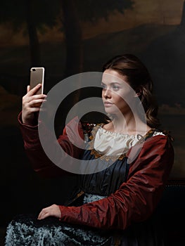 Old and new, concept. Beautiful young Renaissance style woman taking selfie on phone.