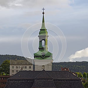 An old Norwegian Church with an ornate copper weathered tower sits at the waterfront on the coastal town of Bergen in Norway.