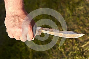 Old notch knife in man`s hand on grass background