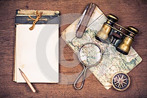 Old notebook, compass, map, vintage binoculars, pencil, knife, magnifying glass on wooden desk background