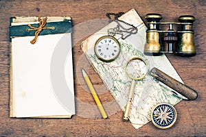 Old notebook, compass, map, vintage binoculars, pencil, pocket watches, knife, magnifying glass on wooden background