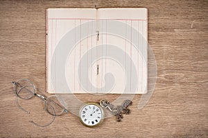 Old notebook, retro eye glasses and vintage pocket watches on oak textured wooden table background