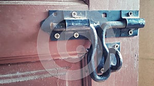 Old nut bolt and iron door lock on faded red colored wood door.