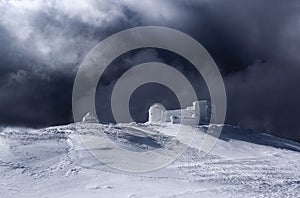 The old observatory covered with textured snow. Dramatic stormy sky with gray clouds. Winter scenery. Beautiful landscape of high