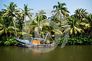 Old ocean fishing boat along the canal Kerala backwaters shore with palm trees between Alappuzha and Kollam, India photo