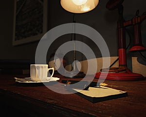 Old office table with fountain pen, notepad, coffee cup, lamp, clock, red candlestick telephone and books.