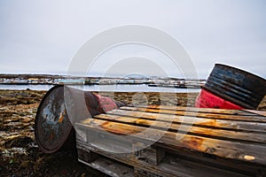 Old oil barrels in a field covered in the grass surrounded by a river under a cloudy sky in Iceland