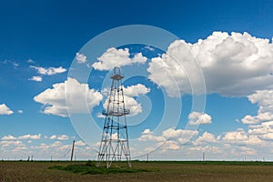 Old oil and gas rig profiled on blue sky with white clouds, in spring