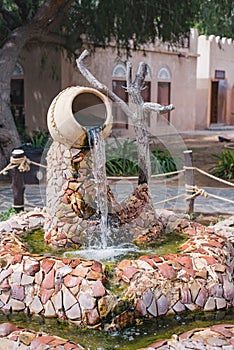 An old oil lamp hangs on a canopy of palm leaves, against the backdrop of a tropical village and palm trees