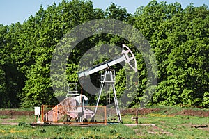 An old oil pump pollutes nature right in the middle of a green forest. photo