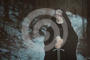 Old one eyed man with sword in dark forest