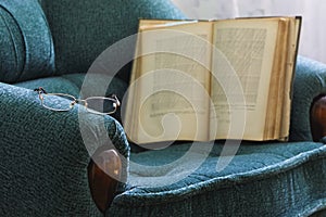 Old open book with glasses on vintage furniture.