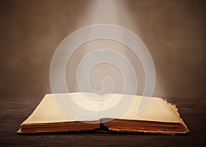 Old open book on a wooden table light beam illuminates the page