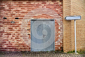 Old orange brick wall with metal sheet door and indicator sign with the inscription erased