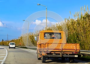 Old orange farm utility vehicle - truck on paved country road in Greece driving to the side so someone can pass