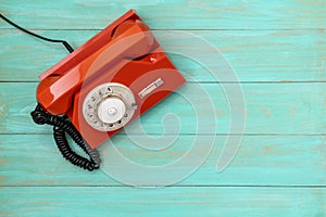 Old, orange rotary dial telephone on blue wooden background