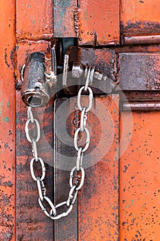 Old orange rusty iron door with lock, metal parts, bolt, nuts and shiny chain. Selective focus