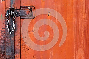 Old orange rusty iron door with lock, metal parts, bolt, nuts and shiny chain. Selective focus